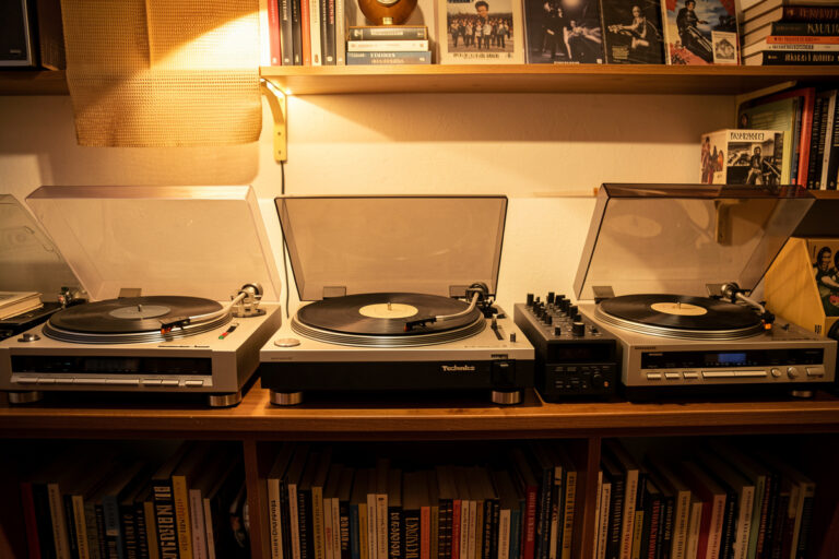 A row of vintage turntables on a shelf including a Technics direct drive and classic belt drive decks