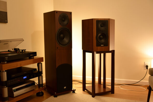 Floorstanding tower speaker beside a bookshelf speaker on a stand in a vinyl listening room