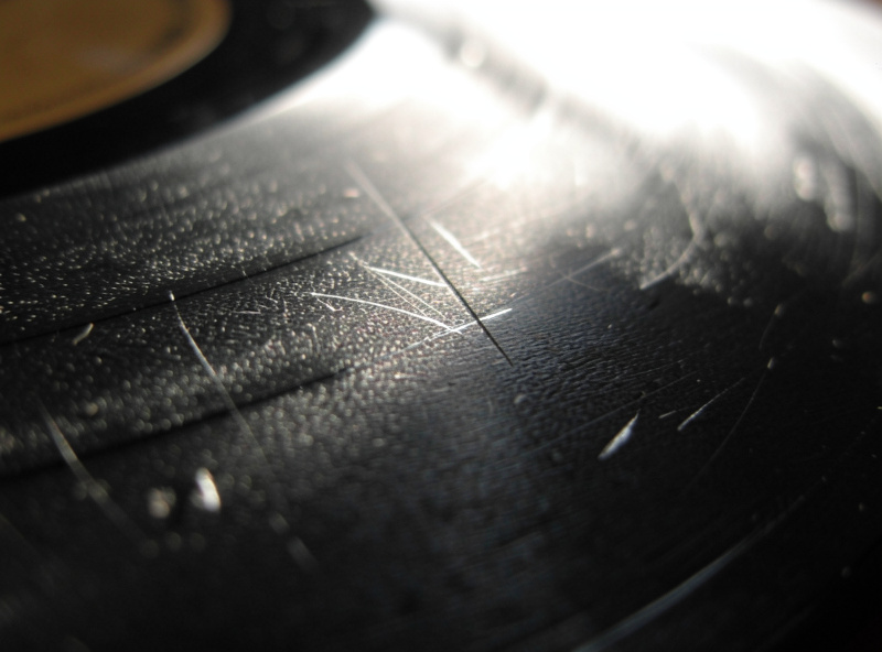 Vinyl record tilted under raking light revealing surface scuffs and scratches