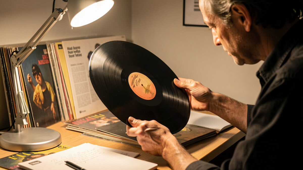 Person grading a vinyl record by holding it up to an angled lamp to inspect the surface