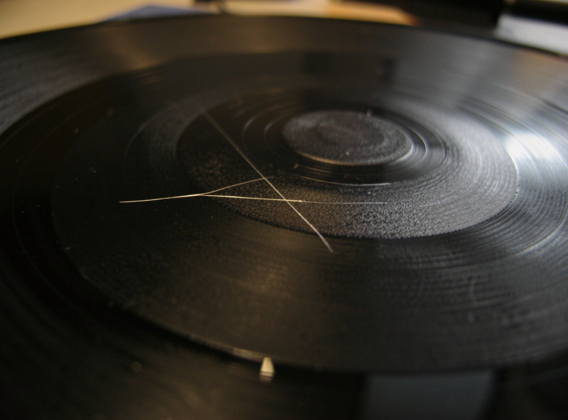 Vinyl record under raking light showing a scratch crossing the grooves