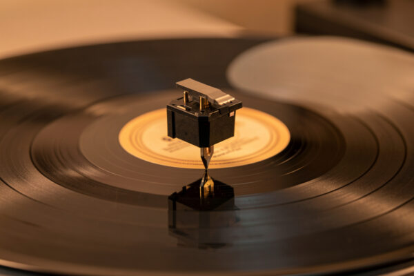A phono cartridge viewed head-on over a record with the stylus vertical and a mirror on the platter