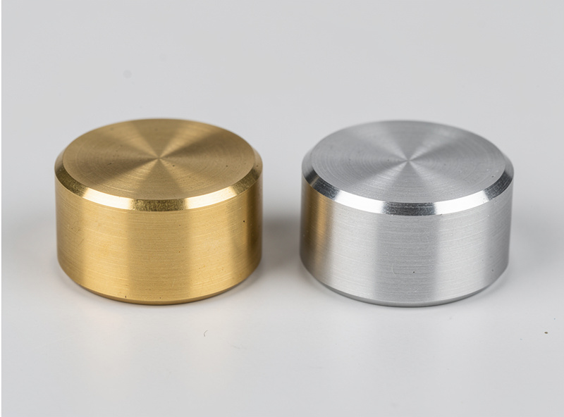 Two record weights side by side, one brass and one aluminum, precision machining and concentric chamfers visible, product comparison photography