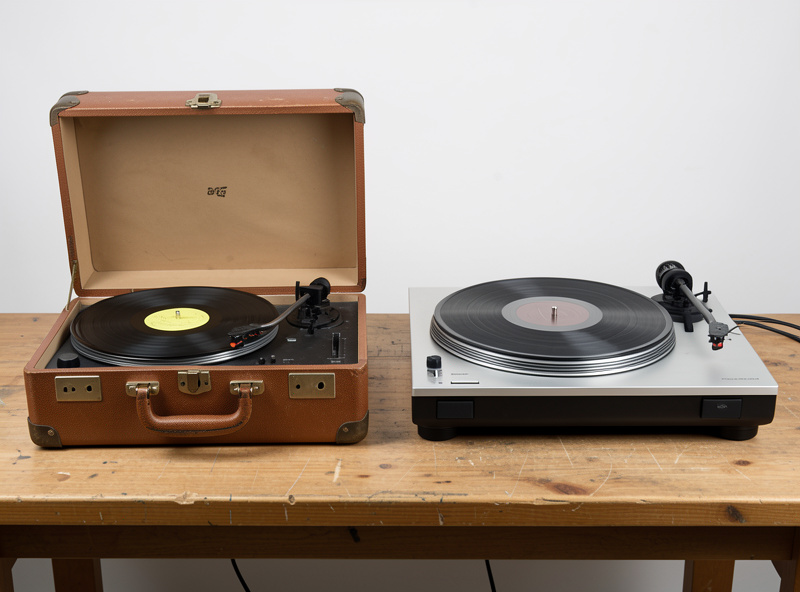 Side-by-side comparison of a cheap briefcase-style record player and a proper entry-level turntable on a workbench