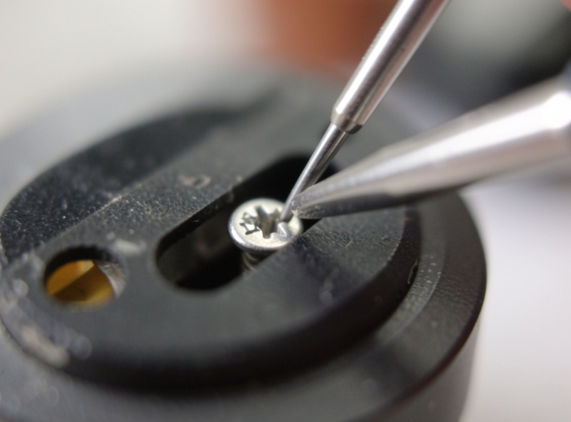Small screwdriver threading an M2.5 screw through a headshell slot into a phono cartridge body