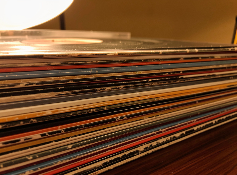 Stack of vinyl records with visible dust and groove wear under warm lamp light