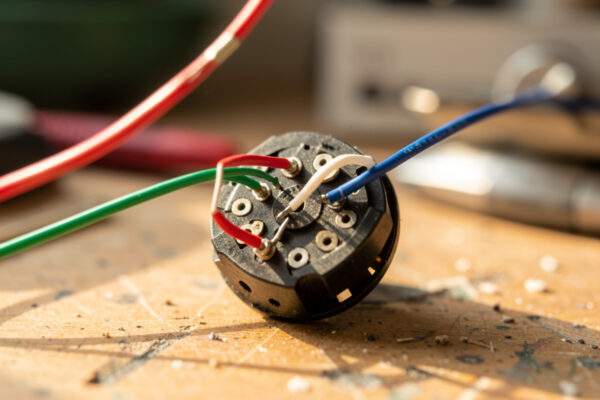 Phono cartridge with red, green, white, and blue headshell lead wires clipped to its pins