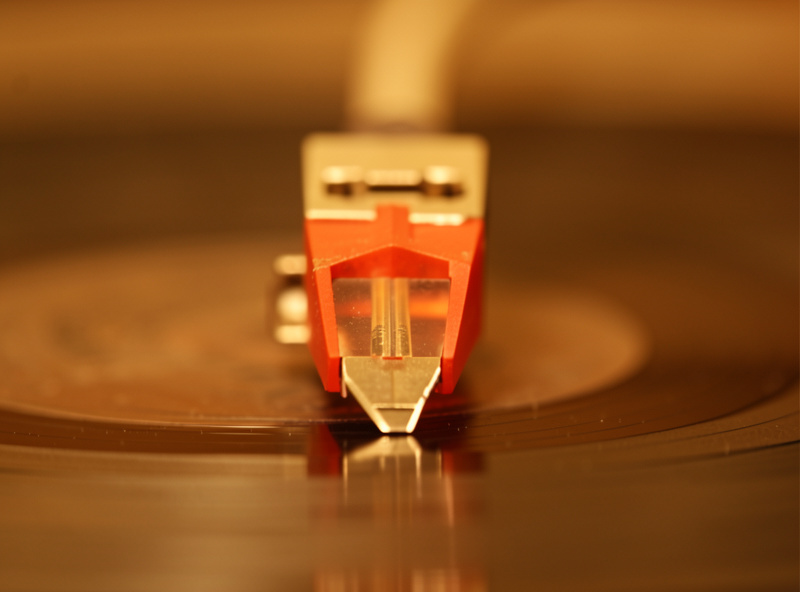 A phono cartridge viewed head-on showing stylus azimuth tilt relative to the record surface
