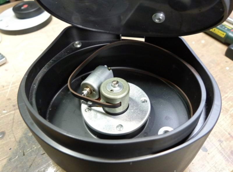 Close-up of a small DC motor and thin drive belt inside an opened portable turntable