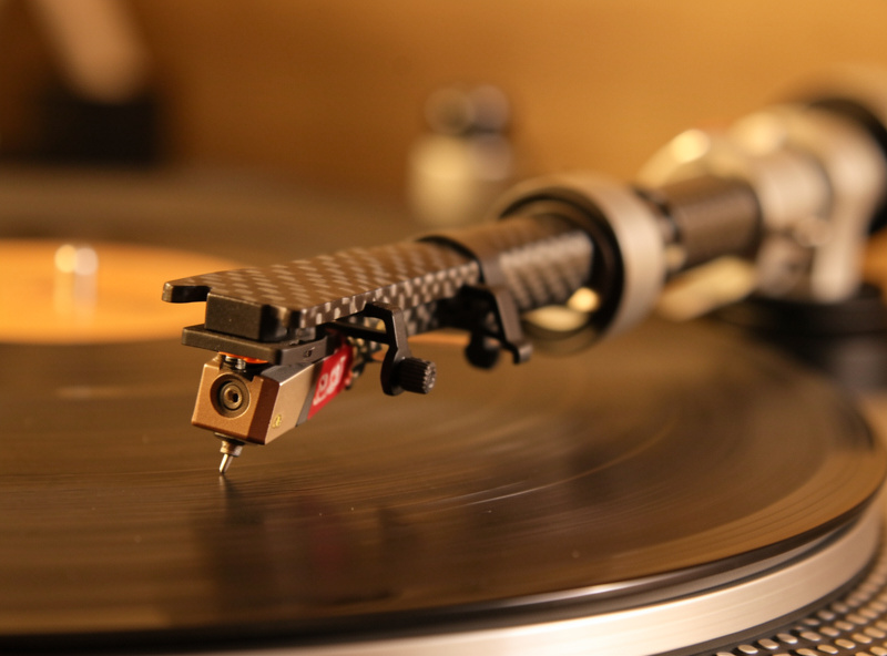 Close-up of a carbon-fiber tonearm tube and headshell with a mounted cartridge on a belt-drive turntable