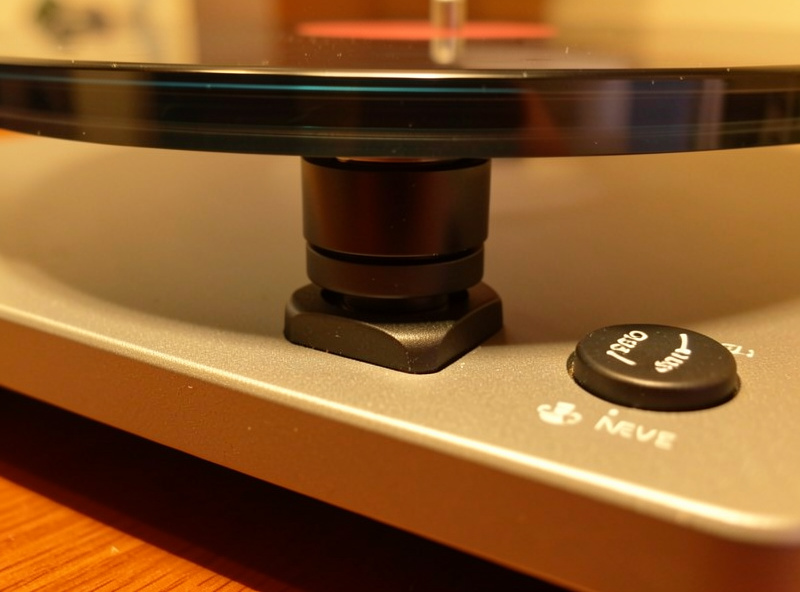 Close-up of height-adjustable turntable feet and an electronic speed control button on a turntable plinth