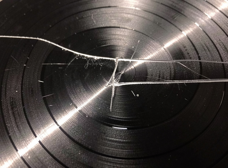 A record spinning on a turntable platter with a visible radial scratch catching the light