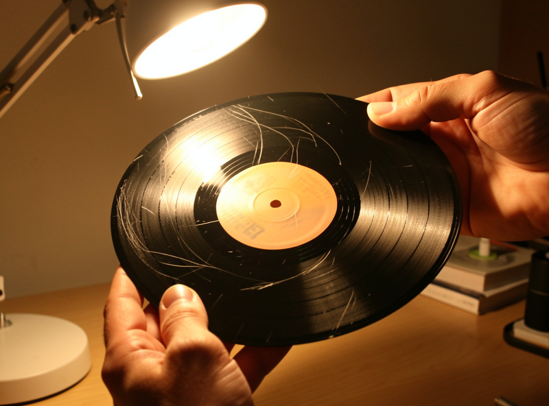 A record held at a raking angle under a bright light to reveal a scratch