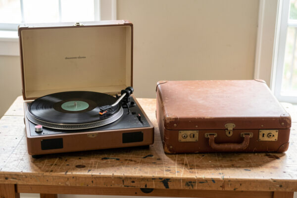 A proper turntable with adjustable tonearm beside a closed suitcase record player on a workbench