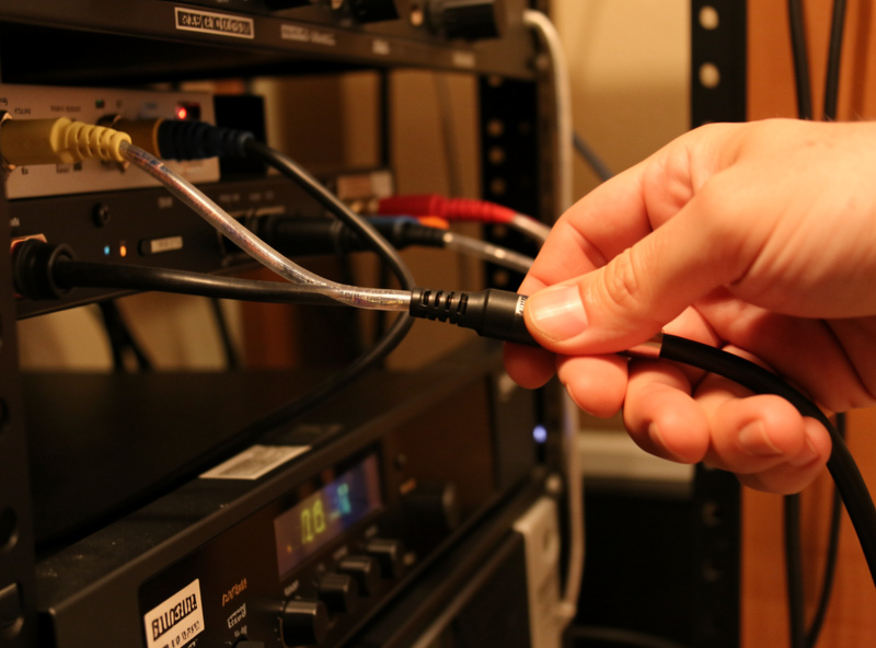 Hand routing an RCA interconnect cable away from a power supply behind a hi-fi rack